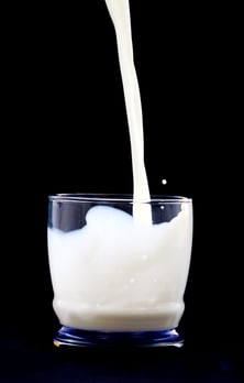 milk being poured in a glass over a black background