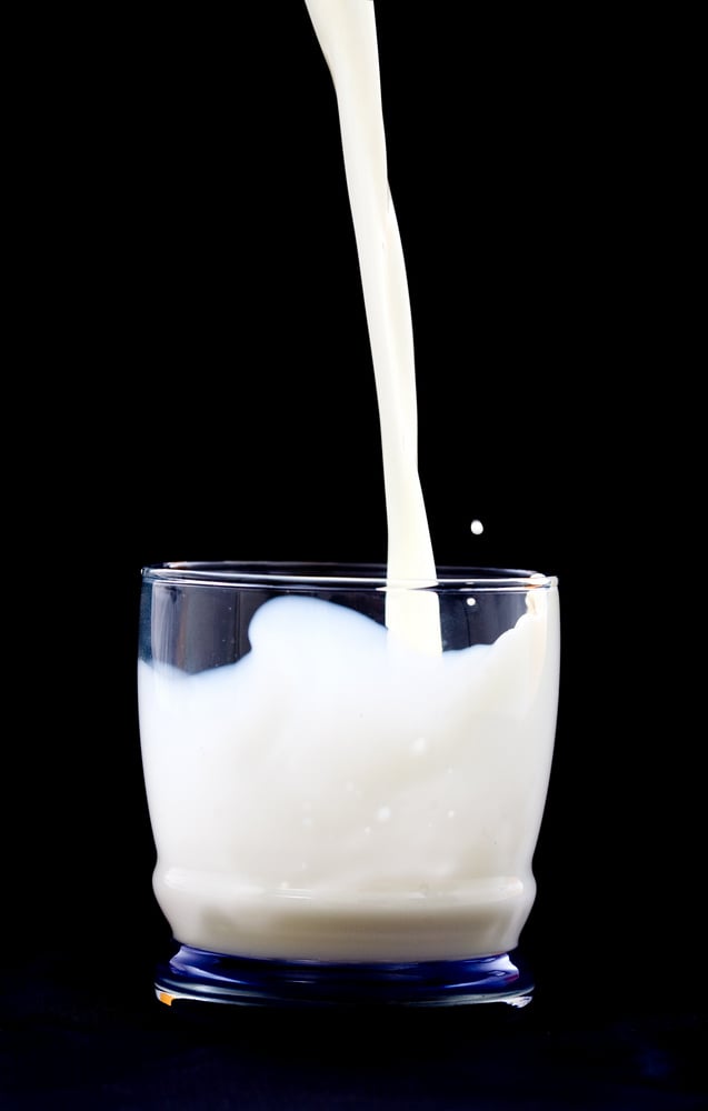 A glass with milk being poured into it.